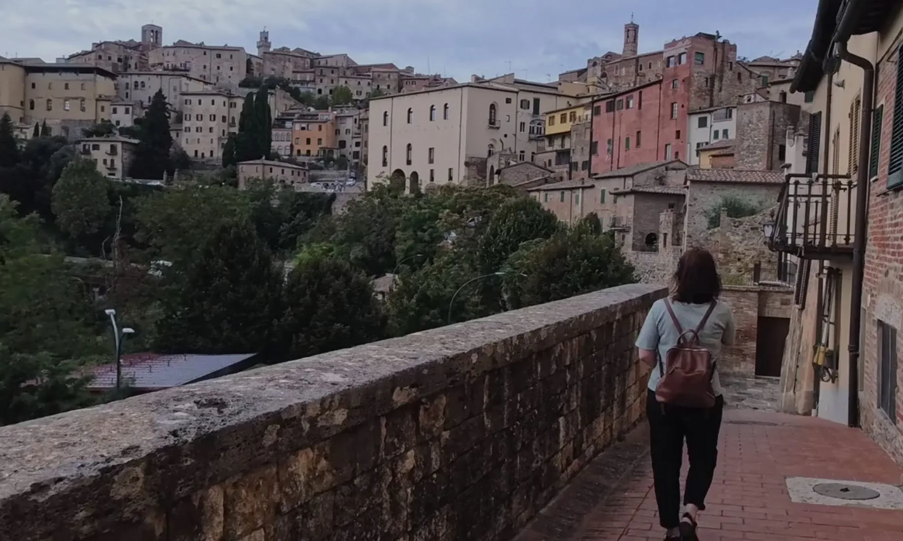 A woman walking a stone path above an Italian hill town at dusk