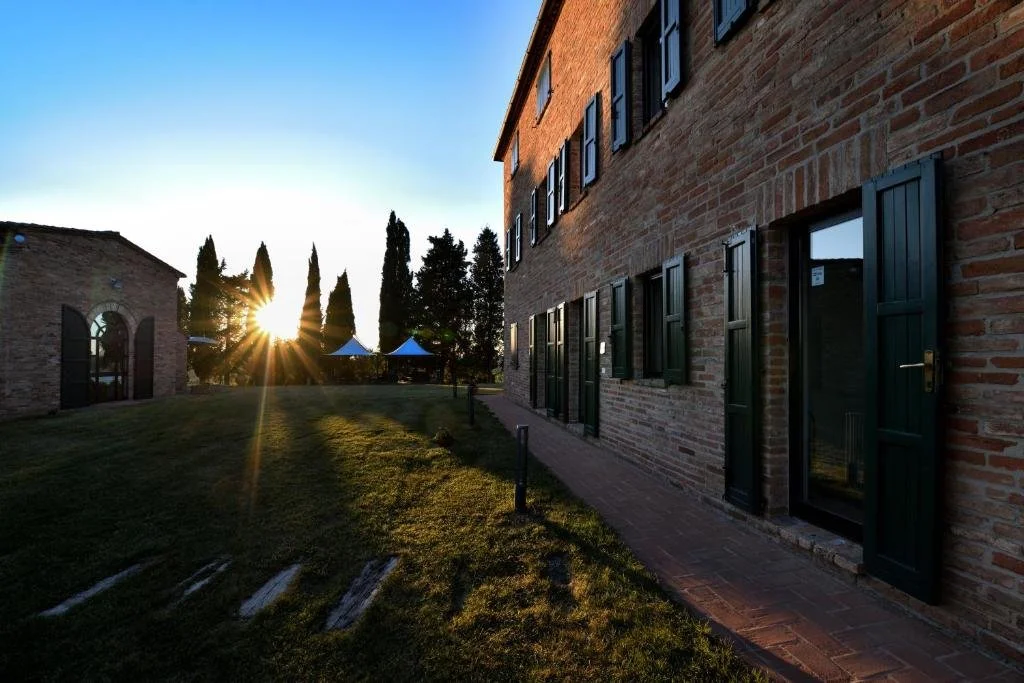 The country house at golden hour, sun flaring through the cypresses